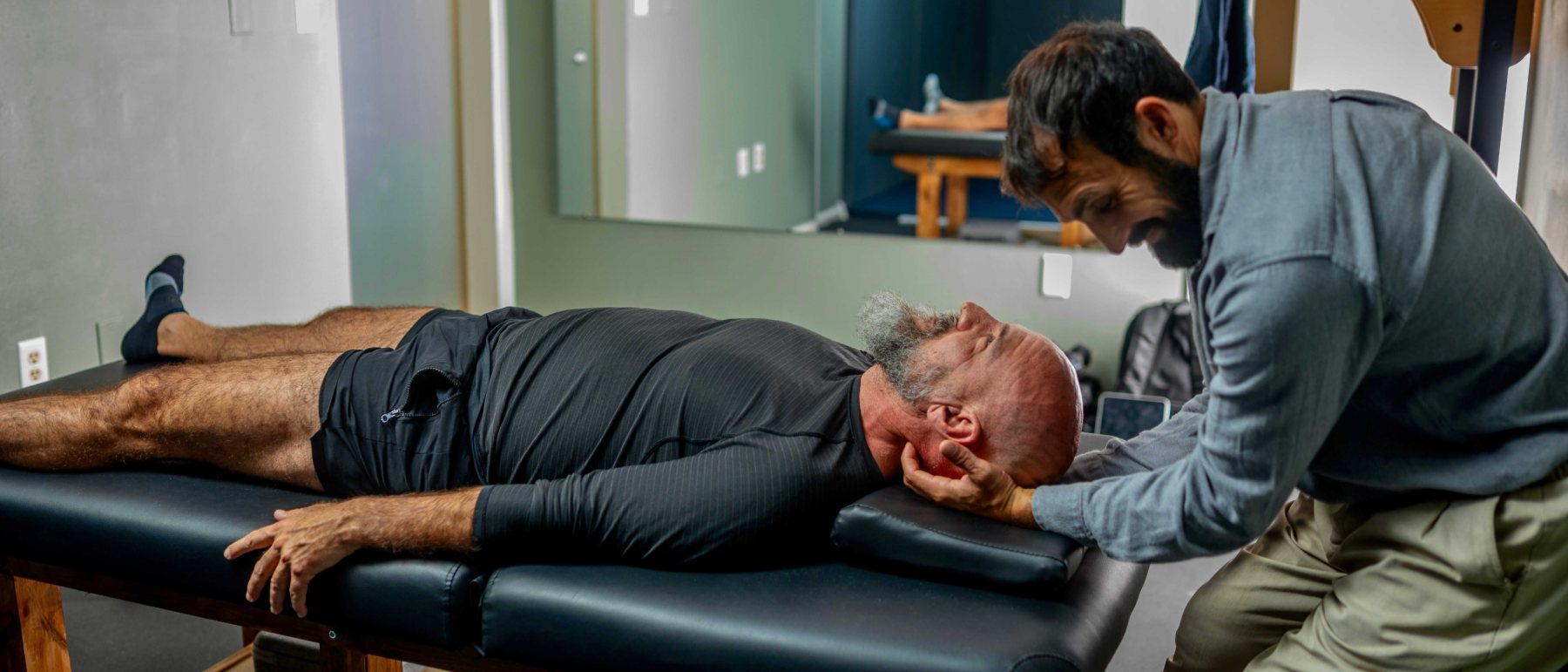 Dr. Lucas Bianco working on a member\u2019s neck and shoulders on the treatment table.